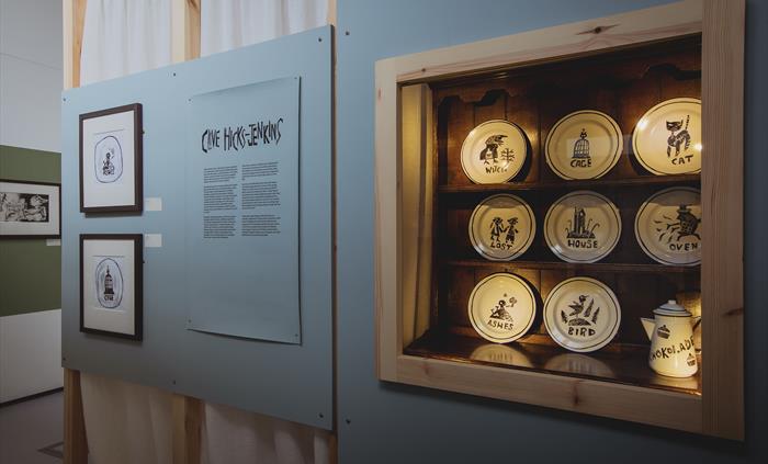 a set of eight enamel plates with illustrations, lit in a display case.
